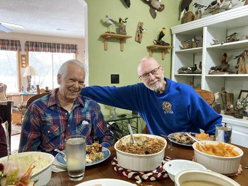 Two men sitting at a table with food
AI-generated content may be incorrect.