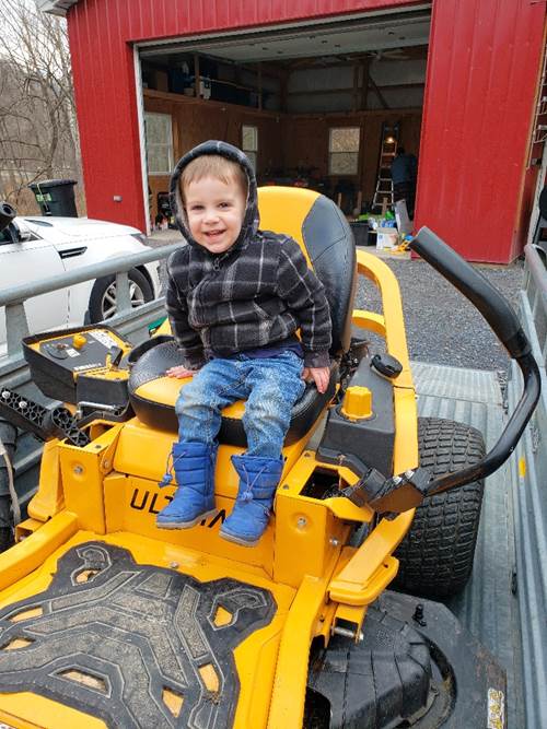 A child sitting on a yellow and black tractor

Description automatically generated