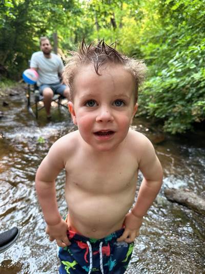 A child standing in a stream with a person sitting on a chair

Description automatically generated